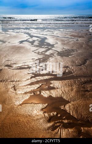 Sable scintillant rivulets forment des motifs abstraits sur la plage. Banque D'Images