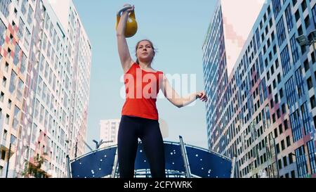 Jeune athlète féminine en plein air, en train de s'entraîner avec une kettlebell. Style de vie sain, entraînement rapide avec une kettlebell à la maison. Banque D'Images