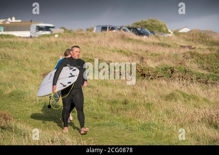 Des surfeurs matures portant leurs planches de surf et marchant avec impatience le long d'un sentier sur Pentire point East à Newquay, en Cornouailles. Banque D'Images