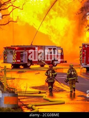 Deux premiers intervenants de la caserne de pompiers locale se rendent vers un moteur d'incendie contrôlant un incendie massif d'une éruption de ligne de gaz naturel. Banque D'Images