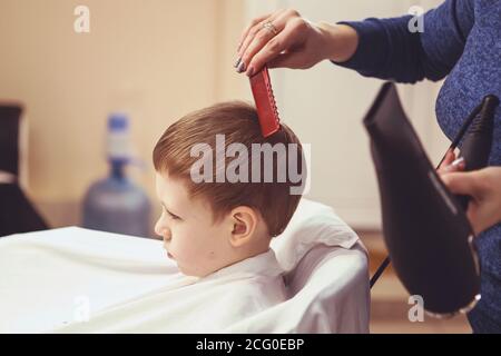 Petit garçon au coiffeur. L'enfant a peur des coupes de cheveux. Les mains de coiffeur faisant la coiffure de petit garçon, gros plan Banque D'Images