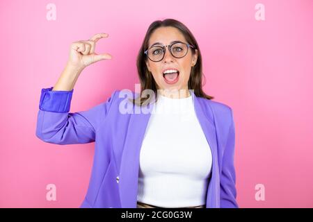 Jeune belle femme d'affaires sur fond rose isolé souriant et confiance gestante avec la main faisant le petit signe de taille avec les doigts regarder et Banque D'Images