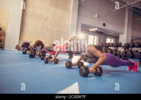 Groupe d'adultes effectuant des exercices de poussée sur des haltères à l'aire d'entraînement physique intérieure avec entraînement multidisciplinaire et lumière vive évasement Banque D'Images