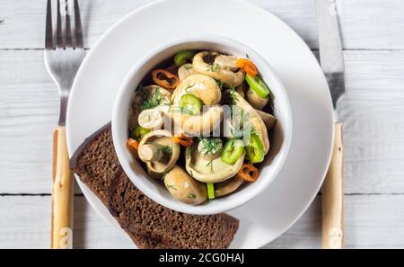 Champignons blancs marinés ou salés avec poivrons et herbes un bol sur une table en bois blanc Banque D'Images