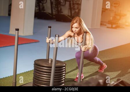 Une jeune femme musclée et forte pousse l'équipement d'exercice du prowler sur gazon artificiel. Faites de la musculation à la salle de sport Cross Fit Gym. Banque D'Images