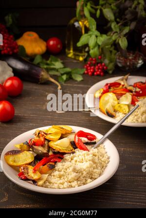 Couscous de porridge avec légumes cuits au four, courgettes et oignons, poivrons et aubergines avec épices, assiette avec nourriture sur fond de bois sombre Banque D'Images