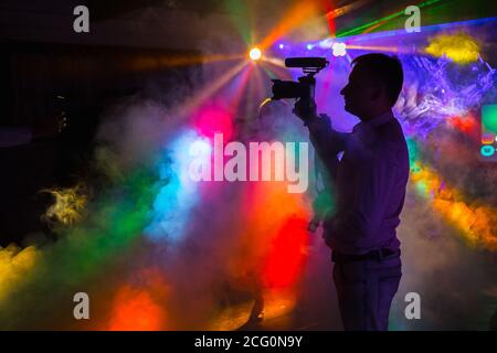 un homme avec une caméra enregistre une vidéo à un discothèque avec des rayons de néon Banque D'Images