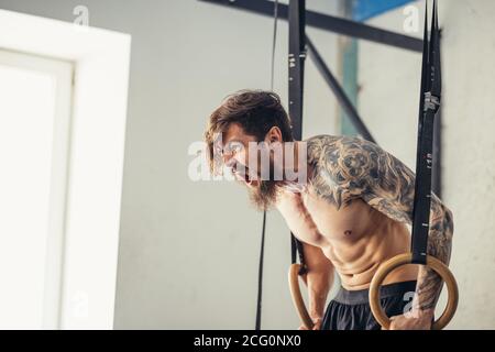 Jeune homme en forme de barbe à embout taté tirant sur des anneaux de gymnastique. Banque D'Images