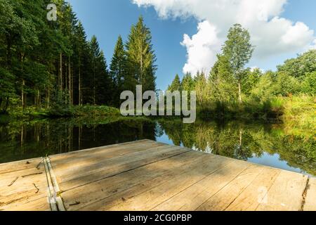 Petit lac avec une jetée en bois dans les Ardennes belges et parc Eifel de la province de Liège près de Bayehon. L'eau donne des reflets étonnants Banque D'Images