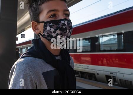 Gros plan d'un enfant caucasien de sexe masculin portant un masque facial pour protéger l'infection par le coronavirus. Il attend debout à la gare. Banque D'Images