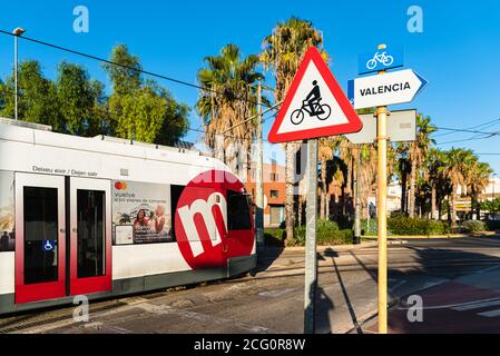 Valence, Espagne - 7 septembre 2020 : un tramway traverse la route tandis que deux touristes cyclistes attendent au feu de circulation pour traverser la rue sur une piste cyclable. Banque D'Images