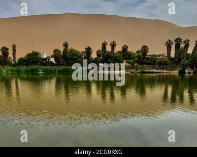 Paysage désertique. Oasis Huacachina au Pérou. Pittoresque lac naturel désertique entouré de hautes dunes de sable. Dune de sable jaune, palmiers verts. Banque D'Images