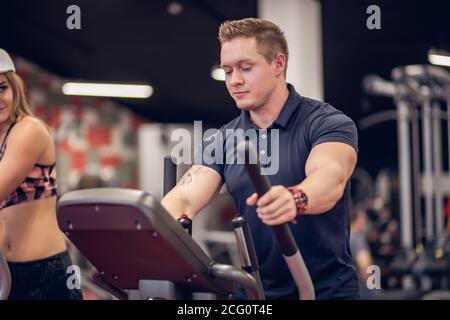 Vue de côté portrait de transpiration fit woman exerçant à l'aide d'une machine elliptique au cours d'entraînement intense dans la salle de sport moderne Banque D'Images