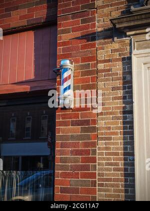 Un poteau de barbier traditionnel rouge, blanc et bleu à l'extérieur d'un bâtiment en brique dans une petite ville américaine. Banque D'Images