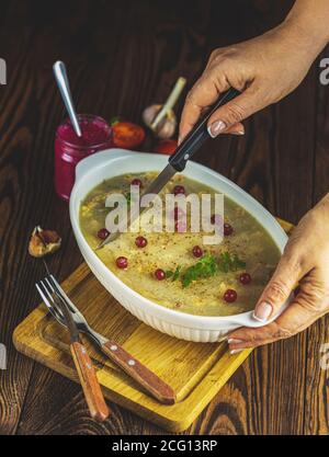 Femme en train de couper de la gelée savoureuse avec de la viande, de l'aspique de boeuf, de la nourriture russe traditionnelle dans un plat blanc, de l'aspique de noël avec des canneberges, des mandarines, du thym Banque D'Images