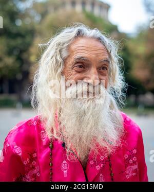 Homme senior portrait d'homme flamboyant souriant barbu avec de longs cheveux blancs portant des vêtements roses dans les rues de Sofia, Bulgarie Banque D'Images