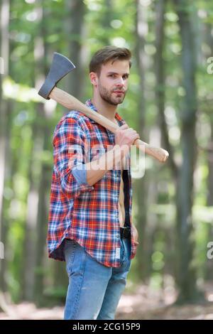 Homme barbu en chemise à carreaux avec jeans porte grande hache en bois d'été environnement naturel, bûcheron. Banque D'Images
