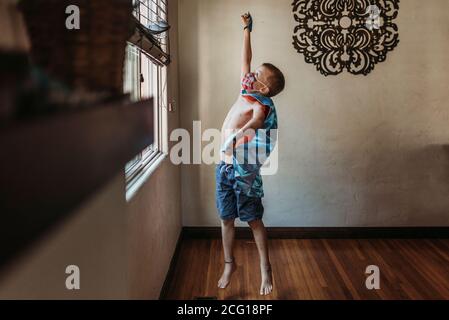 Jeune garçon habillé comme super héros avec le masque debout à côté fenêtre à la maison Banque D'Images