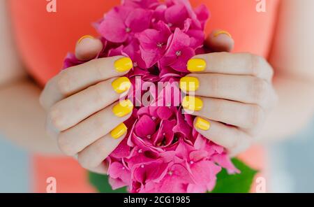 Femmes avec ongles manucurés en jaune tenant une fleur Banque D'Images