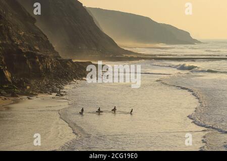 Groupe de surfeurs qui naviguent dans l'océan au coucher du soleil. Banque D'Images