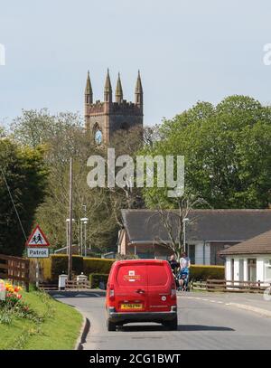 Petite fourgonnette de livraison Red Royal Mail conduite le long de la rue rurale dans le petit village rural d'Irlande du Nord avec des piétons et des prams le jour ensoleillé du printemps. Banque D'Images