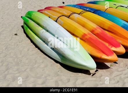 Des kayaks en plastique multicolores, en attente de location par les amateurs de plage, sont empilés sur le sable. Banque D'Images