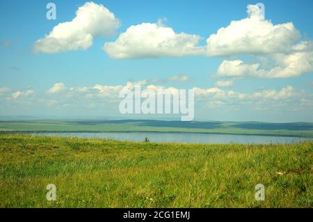 Longue steppe et plusieurs petites maisons sur le flanc d'une colline sur le rivage d'un grand lac pittoresque. Lac de Fyrkal, Khakassia, Sibérie du Sud, Russie. Banque D'Images