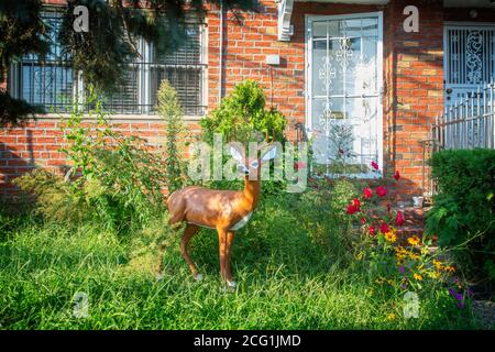 Une statue de cerf se dresse au milieu des fleurs et des mauvaises herbes dans la cour avant d'une maison à Queens, New York Banque D'Images