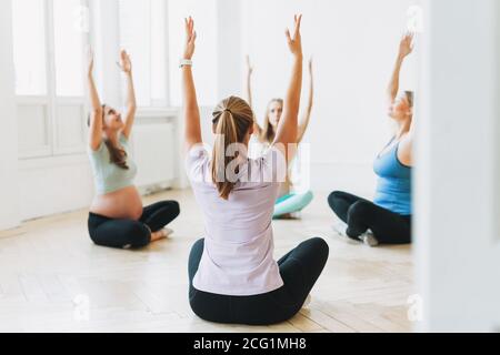 Groupe de femmes enceintes en uniforme de sport avec entraîneur faire gymnastique en studio lumineux Banque D'Images