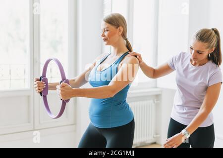 Femme enceinte en uniforme de sport avec entraîneur faisant de la gymnastique dans studio lumineux Banque D'Images