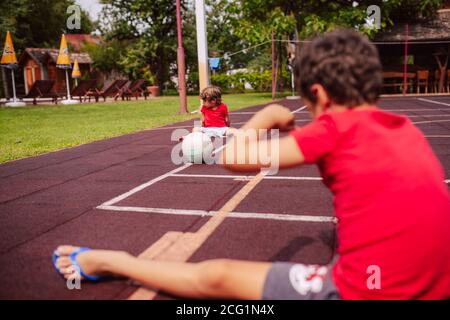 Deux petits garçons caucasiens en T-shirts rouges lancent une balle sur l'aire de jeux. Jeu pour enfants sur le terrain Banque D'Images