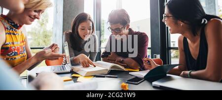 Les jeunes étudiants assis à une table dans une bibliothèque et lisant des livres pour leur affectation en classe. Étudiants de l'université qui font des études de groupe en bibliothèque. Banque D'Images