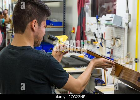 Ouvriers construisant et assemblant des guitares à l'usine Taylor Guitar de Tecate, au Mexique. Ce travailleur règle la barre de treillis dans le cou de la guitare. Banque D'Images