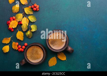 Deux tasses en argile brune de café noir, des branches avec de petites feuilles d'automne (Spiraea Vanhouttei) et des fruits rouges de Rowan sur bois peint bleu-vert foncé Banque D'Images