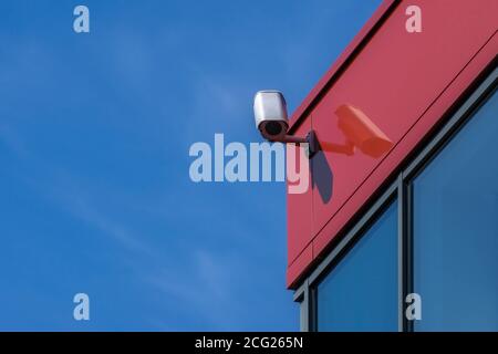 Caméra de vidéosurveillance installée sur un mur rouge moderne. Caméra de sécurité sur fond bleu ciel avec espace de copie. Sécurité extérieure de l'équipement vidéo Banque D'Images