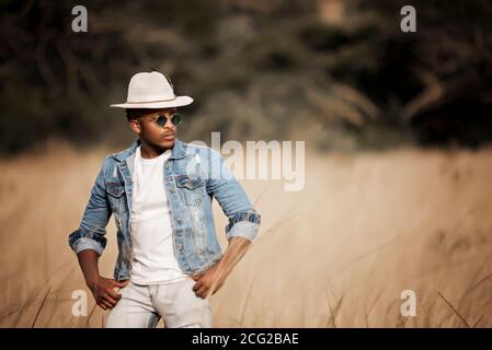 homme africain dans le bush africain portant un chapeau et lunettes de soleil au soleil éclatant Banque D'Images