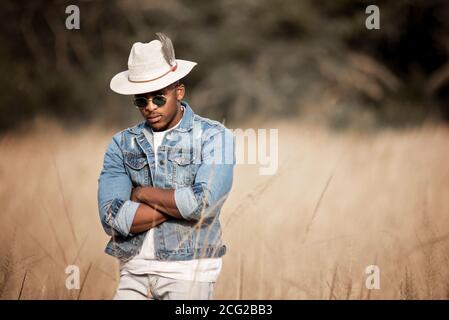 homme africain dans le bush africain portant un chapeau et lunettes de soleil au soleil éclatant Banque D'Images