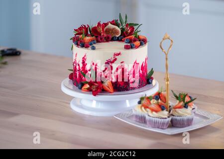 Grand beau gâteau de velours rouge, avec fleurs et baies sur le dessus. Délicieux muffins sucrés à la crème, décorés de fraises et de bleuets. Banque D'Images