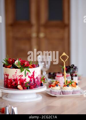 Grand beau gâteau de velours rouge, avec fleurs et baies sur le dessus. Délicieux muffins sucrés à la crème, décorés de fraises et de bleuets. Banque D'Images