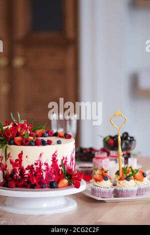 Grand beau gâteau de velours rouge, avec fleurs et baies sur le dessus. Délicieux muffins sucrés à la crème, décorés de fraises et de bleuets. Banque D'Images