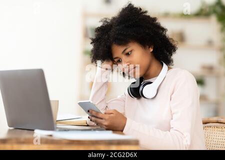 African Girl utilisant un smartphone et un ordinateur portable regardant la lecture à la maison Banque D'Images