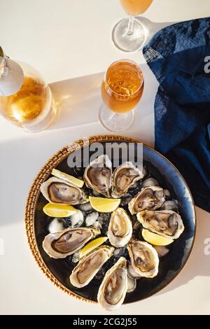 Assiette d'huîtres fraîches avec vin mousseux citron et rose sur la table blanche, vue du dessus Banque D'Images