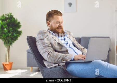 Travailler en ligne au bureau à domicile. Un homme de graisse drôle travaille avec un ordinateur portable dans la chambre d'appartement.