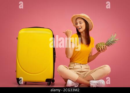 Fille avec ananas pointant à la valise, aller vacances Banque D'Images