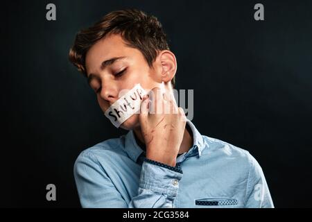 Le concept de violence domestique. Un adolescent, avec sa bouche collée, ferme une bande adhésive avec les mots fermés avec ses mains rayées. Fond noir Banque D'Images