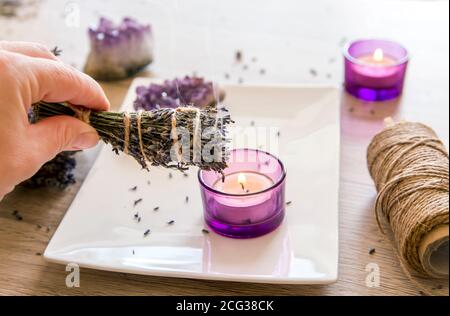 Personne tenant des herbes maison lavande (lavendula) bâton de taches avec la fumée sortant, des bougies et des amas de cristal améthyste pour la décoration. Banque D'Images