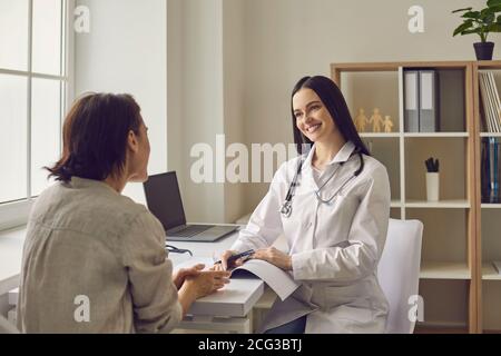 Médecin thérapeute souriant à l'écoute des plaintes de femme patient pendant visite en clinique médicale Banque D'Images