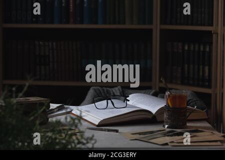 Lunettes sur le livre ouvert et une tasse de thé. Bibliothèques en arrière-plan Banque D'Images