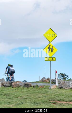 Deux cyclistes mâles se ravirent vers la crête d'une colline, après un panneau Crest sur Dairy Farmers Hill à Canberra, TERRITOIRE DE LA CAPITALE AUSTRALIENNE Banque D'Images