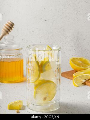 concentration sélective, vitamines naturelles, verre à haute glace pour l'eau, pot transparent avec miel et tranches de citron sur un fond clair Banque D'Images